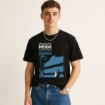 Młody mężczyzna w czarnym T-shircie Depeche Mode Some Great Reward z niebieską grafiką budynku i sylwetkami pary